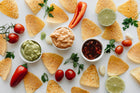 A vibrant spread of Hola Mija Chips, authentic Mexican tortilla chips, surrounded by fresh ingredients like tomatoes, lime, and herbs, served with creamy guacamole and salsa, showcasing the true Mexican flavor without seed oils.